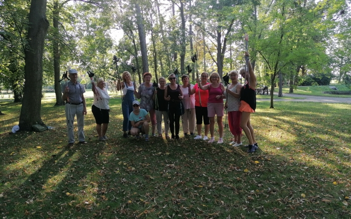 park, wokół zielone drzewa, grupa uczestników wydarzenia pozuje stojąc obok siebie , w rękach trzymają kijki 