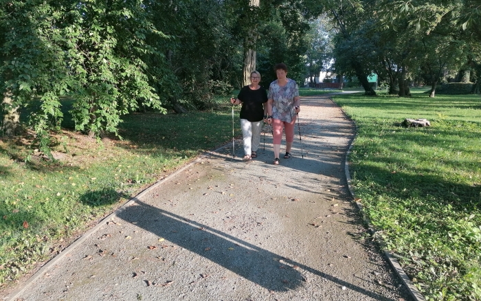 dwie kobiety maszerują z kijami po parkowej ścieżce