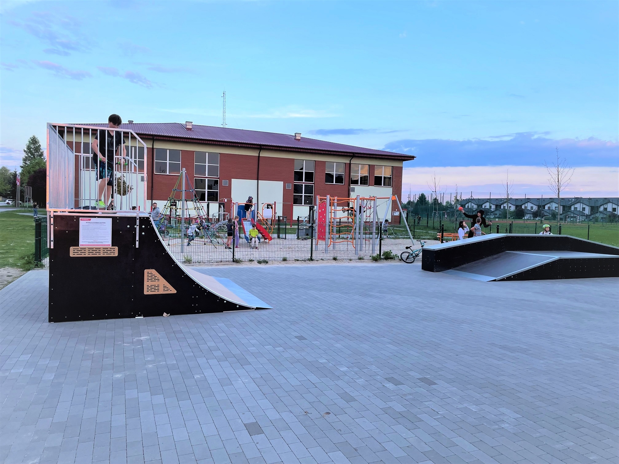 na pierwszym planie urządzenia skyteparku, za nimi plac zabaw i hala sportowa