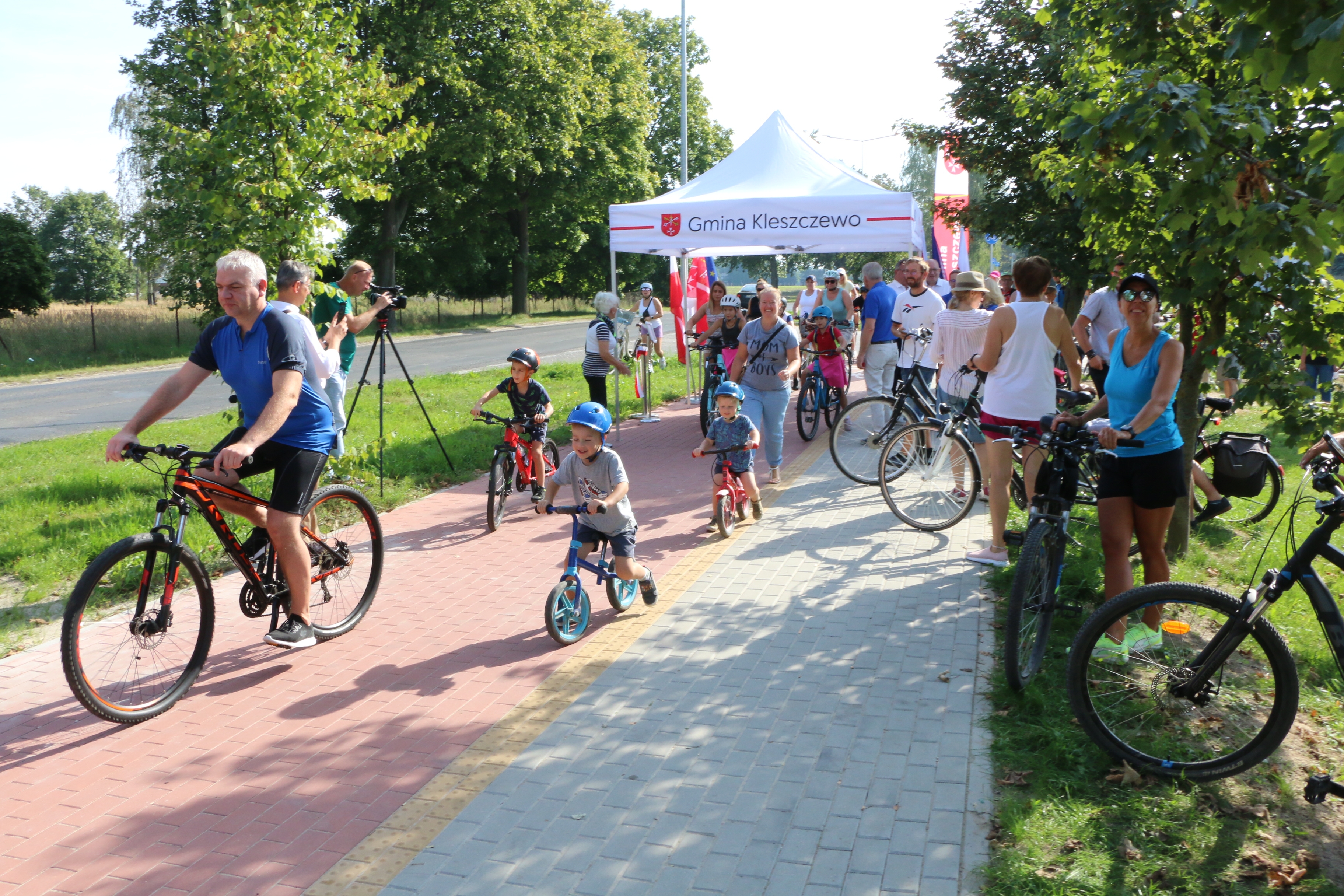 rowerzyści na starcie ścieżki rowerowej, wśród nich dzieci na rowerkach biegowych