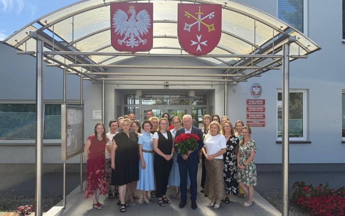 wójt z bukietem kwiatów i pracownikami urzędu przed budynkiem urzędu