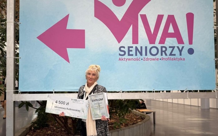 Pani Mirosława Rutkowska z dyplomem i nagrodą na tle baneru wydarzenia 