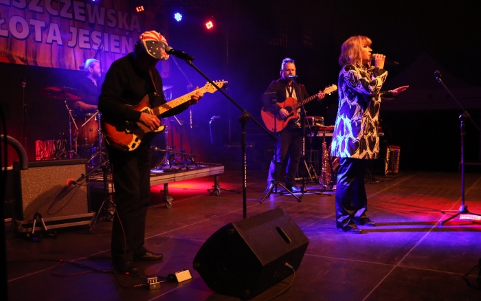 występ zespołu 2 plus 1, na scenie dwóch mężczyzn z gitarami pomiędzy nimi kobieta - wokalistka, za nimi perkusista 