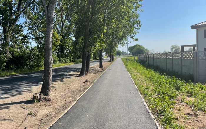 Droga pieszo-rowerowa w Tulcach - kierunek Gowarzewo - widok na ścieżkę pokrytą asfaltem po prawej stronie zabudowania, po lewej pas zieleni z drzewami za  nim  jezdnia 