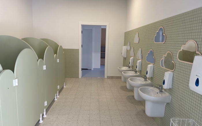 łazienka, po lewej stronie niskie kabiny z toaletami, po prawej stronie umywalki na tle zielonych płytek