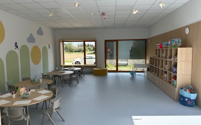 sala przedszkolna,  jasne ściany z kolorowymi akcentami, okrągłe stoliki z krzesłami dla dzieci, pod ścianą półeczki z zabawkami